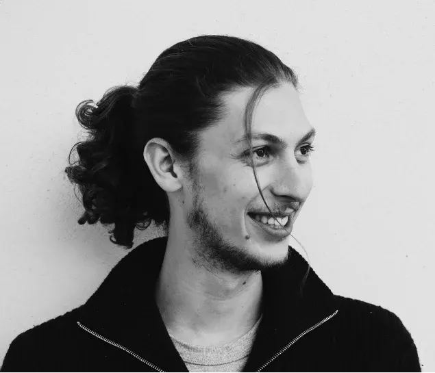 Martin Delahousse, en noir et blanc, sourit en regardant sur le côté.